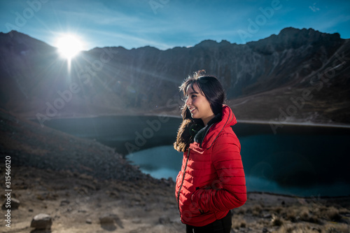 Girl looking at the landscape panorama and smiling on a mound of rocks, wearing a red jacket, behind her is the lake and mountains photo