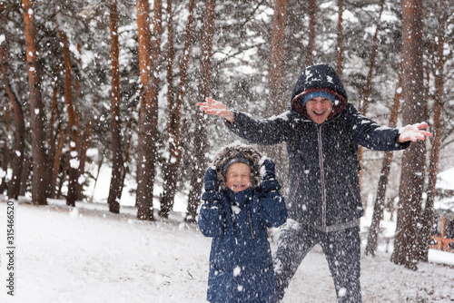 Dad and son rejoice in the falling snow in winter. A family is standing in the forest. There is a place for text on the left of the frame. Happy national snow day.
