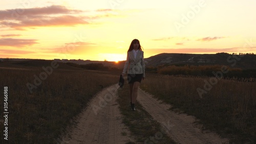sexy Business woman walking along a country road with a briefcase in hand  the sun shimmers at sunset. Sexy business girl working in countryside. beautiful girl travels the countryside.