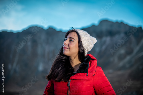 Girl looking at the landscape panorama and smiling on a mound of rocks, wearing a red jacket and a white winter hat, behind her is the lake and mountains photo