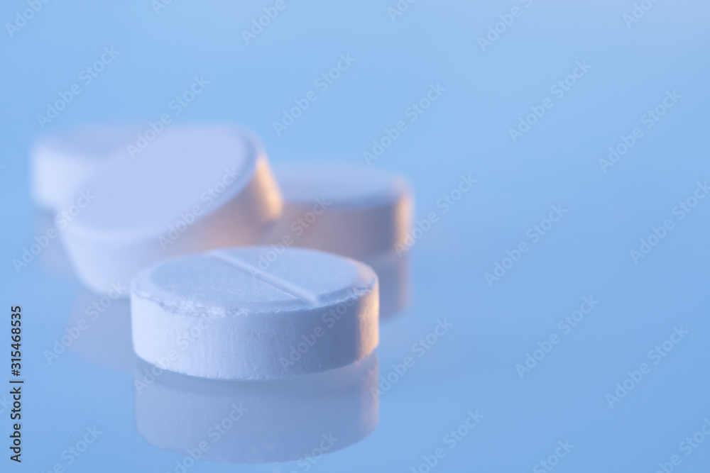 White round pills on a blue mirror surface with copy space, close up. Medicines on glass lit by the morning sun. White round pills on a blue mirror surface with copy space, close up. Medicines on glass lit by the morning sun.