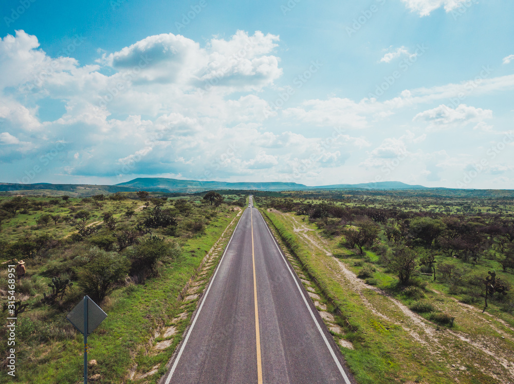 A long straight road with green fields alongside and blue sky A long straight road with green fields alongside and blue sky