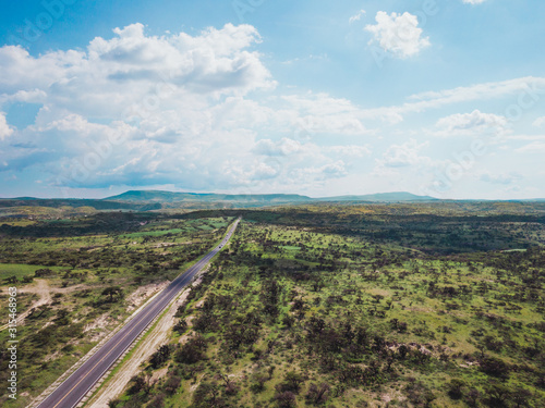 Aerial view of highway in the middle of green fields and blue sky.