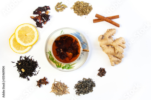 Filiżanka z herbatą otoczona różnymi gatunkami herbat oraz rozgrzewającymi leczniczymi przyprawami i dodatkami do herbaty