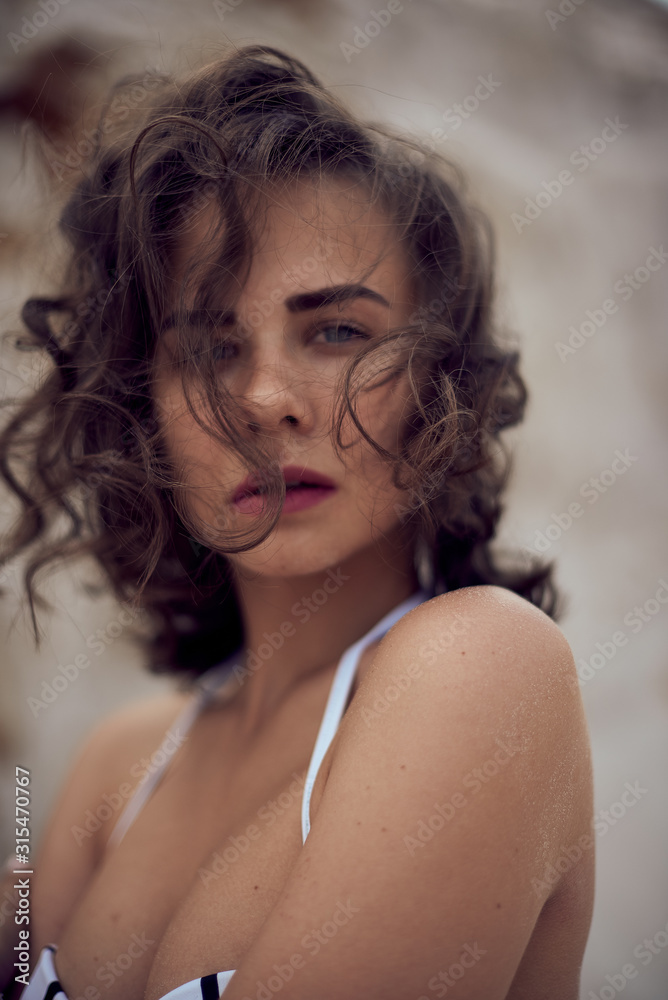 portrait of beautiful caucasian sunbathed woman model with dark long hair in striped swimsuit lying on summer beach with white sand. Top view portrait of beautiful caucasian sunbathed woman model with dark long hair in striped swimsuit lying on summer beach with white sand. Top view