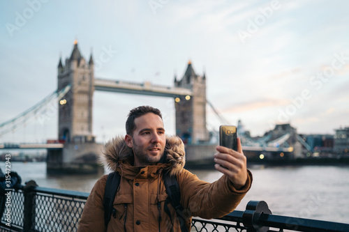 Photography Young Man taking a photo with the smart phone to the Tower Bridge in London on a sunny winter day, London, Great Britain
