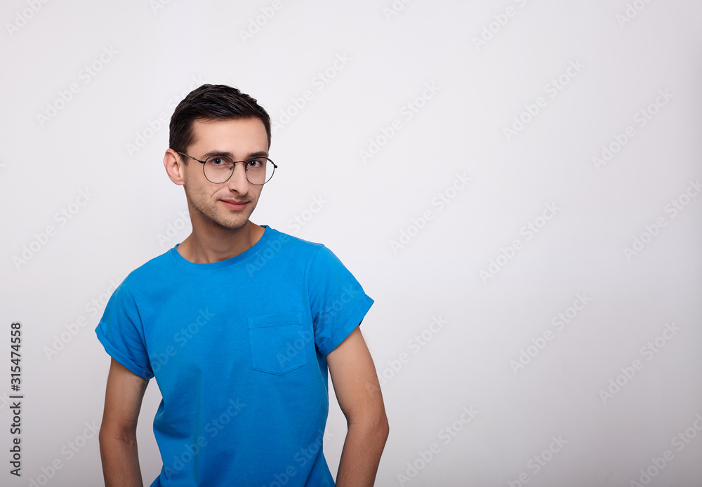 A cute young man with glasses and a blue T-shirt looks straight.