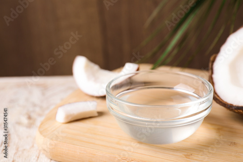 Coconut oil in glass bowl on wooden board, closeup
