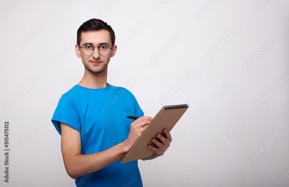 A young man with a notebook in his hands looks into the camera against a white background. A young man with a notebook in his hands looks into the camera against a white background.