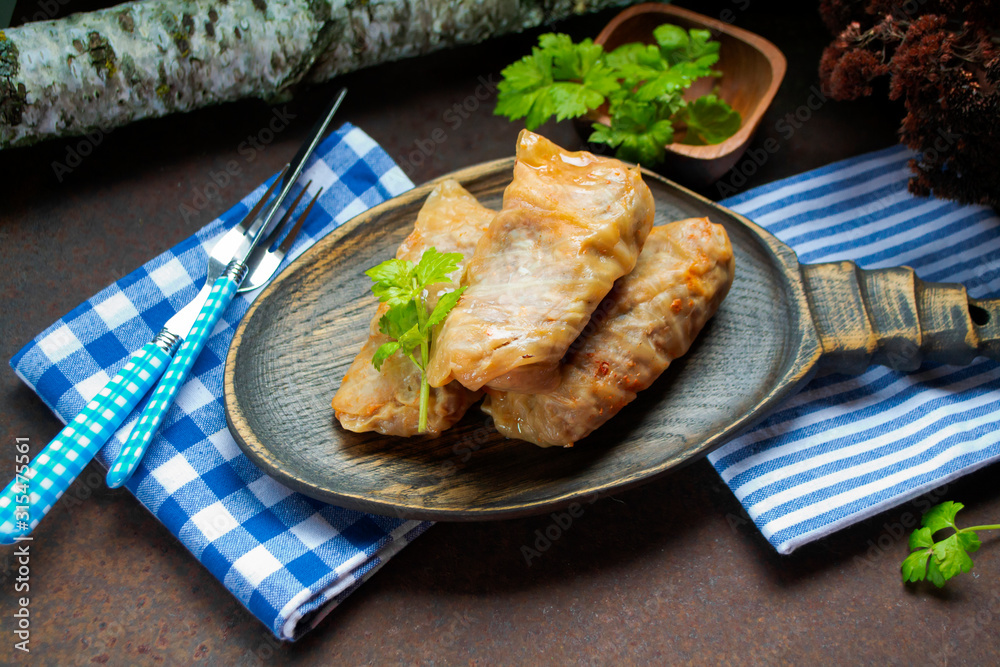 Piping hot baked cabbage rolls with a tomato sauce on wooden plate and rust background