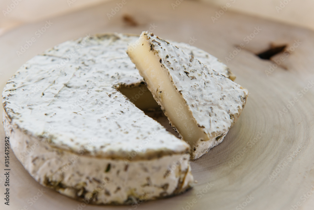 Handmade brie cheese in herbs on wooden table