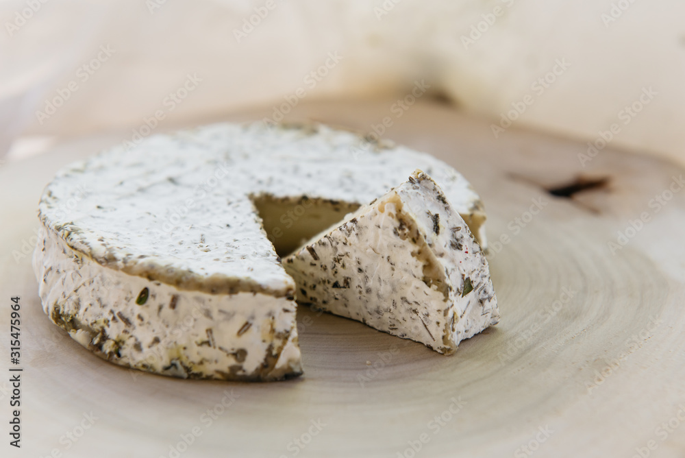 Handmade brie cheese in herbs on wooden table