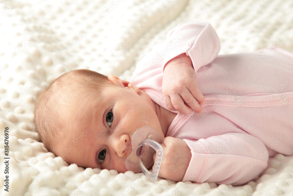 Baby girl lying on white bed and sucks a dummy, top view Baby girl lying on white bed and sucks a dummy, top view