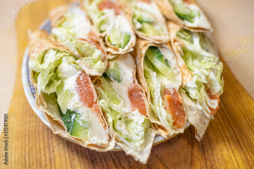 Tortilla rolls with salmon, tender cheese, lettuce and fresh cucumber close-up on a plate