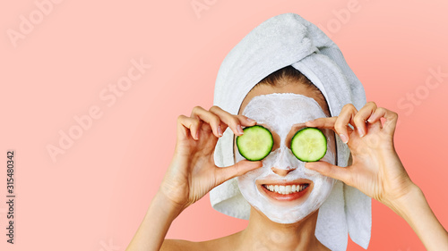 Cosmetology, skin care, face treatment, spa and natural beauty concept. Woman with facial mask holds slices of cucumber.