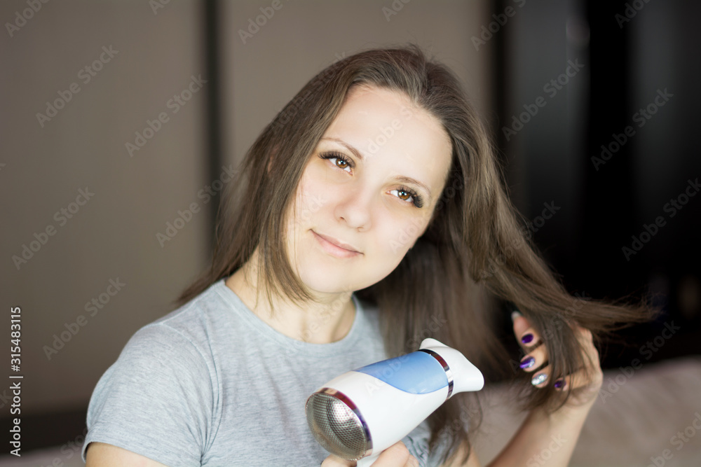 Woman looking at the camera and while drying her hair with hair dryer Woman looking at the camera and while drying her hair with hair dryer