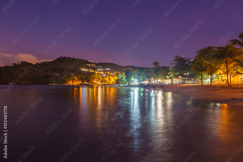 Landscape view of Anse a l’Ane sandy beach with palm trees and calm bay at colorful dusk with peaceful Caribbean sea, Martinique island, Lesser Antilles
