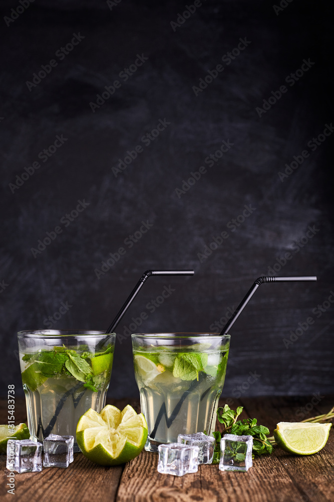 Fototapeta premium Fresh drink with lime, mint and ice on wooden table on dark background. Portrait, vertical format. Copy space.