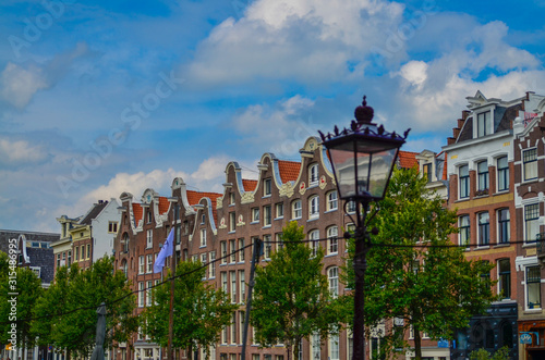 Amsterdam, Holland, August 2019. The typical and charming houses: they are a symbol of the city represented on a postcard. With brightly colored brick facades and distinctive roofs. A lamppost frames.