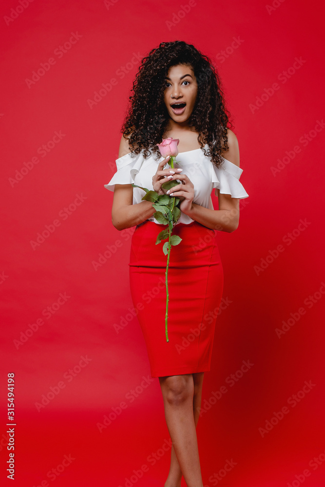 black woman with pink rose smiling and wearing skirt isolated on red background black woman with pink rose smiling and wearing skirt isolated on red background
