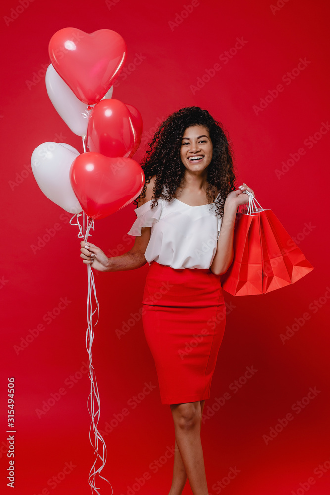 beautiful black woman with colorful heart shaped balloons and shopping bags on red background beautiful black woman with colorful heart shaped balloons and shopping bags on red background