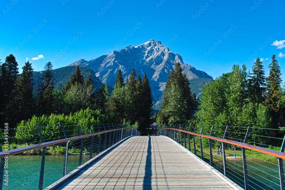Fototapeta premium Bridge leading to Mr. Girouard in Banff, Alberta. Taken during a an early spring day with a beautiful blue sky.