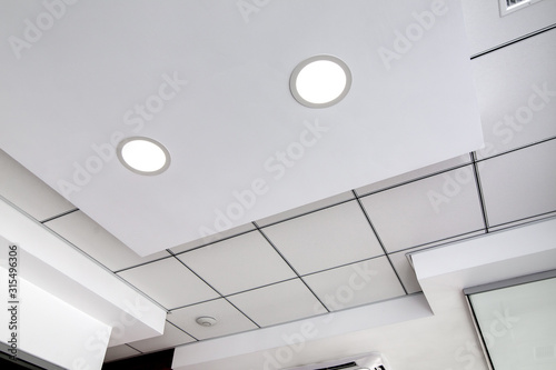 multi-level ceiling with three-dimensional protrusions and a suspended tiled ceiling with a built-in round led light, white color.