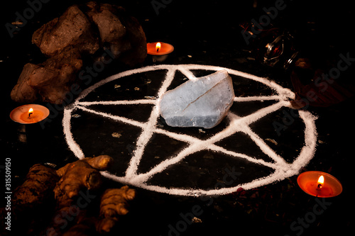 Fotografie Pentagram made of salt, a pagan symbol used for protection by the wiccan community,  surrounded by candles, herbs and spices on a black shiny table top