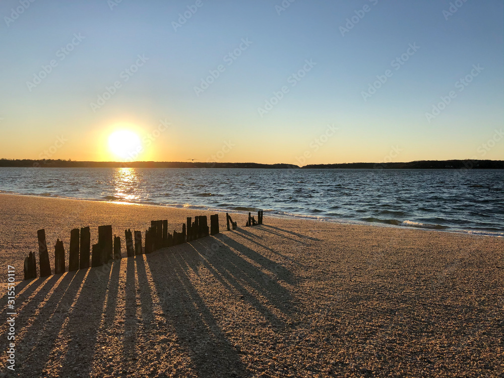 Fototapeta premium Sunset over Hobart Beach Park with remnants of a wood fence in Northport, Long Island, New York.