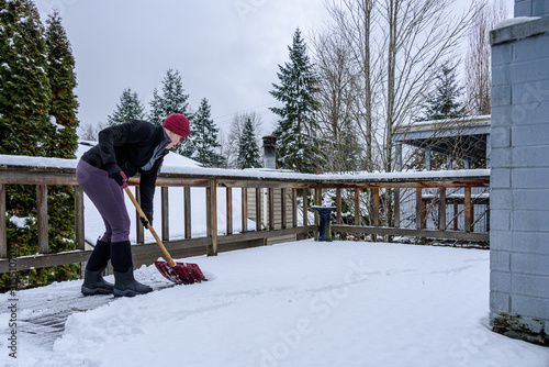 Photography Mature woman shoveling fresh wet snow off a cedar deck railing, snow day
