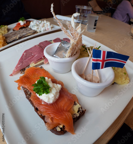 Icelandic food sample platter with fermented shark, dried fish, smoked trout and lamb, with iceland flag on top