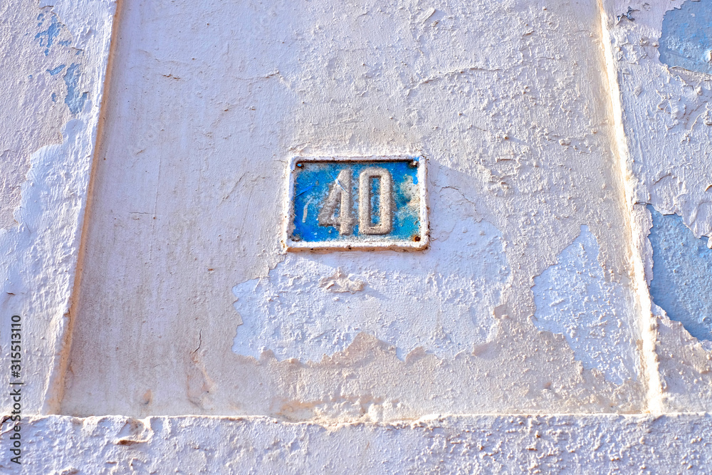 Number 40, forty, blue plate on grungy pink wall with flaking paint.