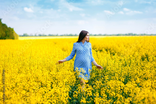 Beautiful pregnant girl walking on a rape field, stylish expectant mother in a blue dress