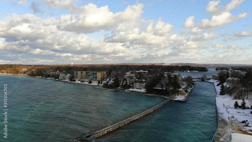 Charlevoix Michigan Pier Lighthouse overlooking Lake Michigan Great Lakes with Fresh Water on a Sunny Winter day with waves looking at downtown hotels condos on lake front property Charlevoix Michigan Pier Lighthouse overlooking Lake Michigan Great Lakes with Fresh Water on a Sunny Winter day with waves looking at downtown hotels condos on lake front property