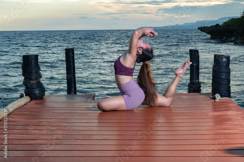 Young beautiful Filipina woman yoga posing on oceanside pierduring tropical sunset 