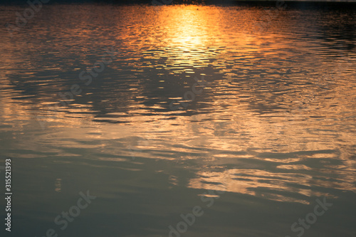 Beautiful abstract golden light sunset reflection on water surface in sunset time. Red and orange light reflection on the lake.