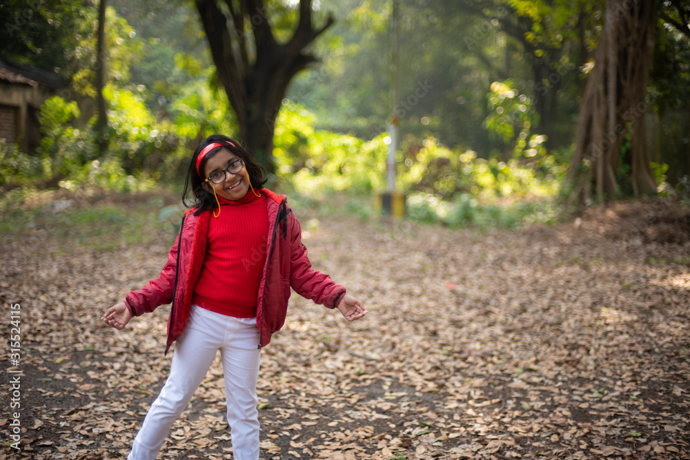 A cheerful Indian Bengali brunette baby girl with red woolen having fun in  dry grass field