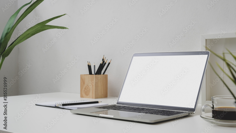 Close up view of workspace with blank screen laptop, coffee cup and pencils on withe desk with white wall Close up view of workspace with blank screen laptop, coffee cup and pencils on withe desk with white wall