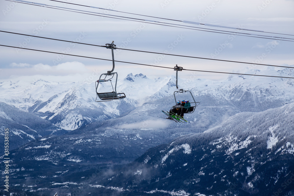 Obraz premium Whistler, British Columbia, Canada. People going up the mountain on a Chairlift during a vibrant and cloudy winter day.