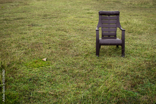 A plastic chair in a green grass field. Empty chair in a park.