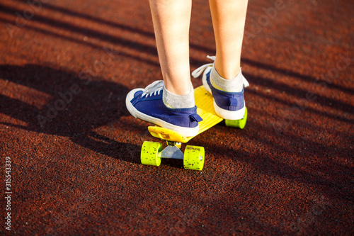 Close up legs in blue sneakers riding on yellow skateboard in motion. Active urban lifestyle of youth, training, hobby, activity concept. Active outdoor sport for kids. Child skateboarding. 