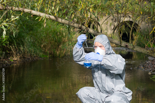 a scientist in a protective suit and mask collects a sample of water in a flask with a blue liquid © kurgu128