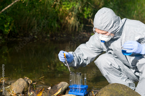 a scientist in a protective suit and mask, takes a sample of liquid from the reservoir into test tubes