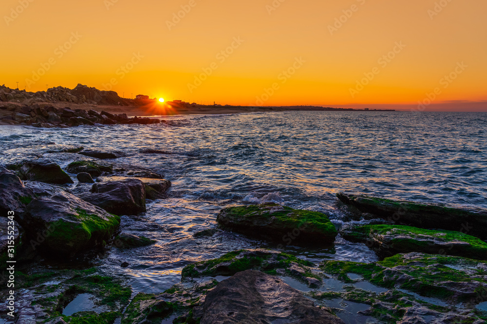 Wave crashing on the rocky seashore at dramatic sunset