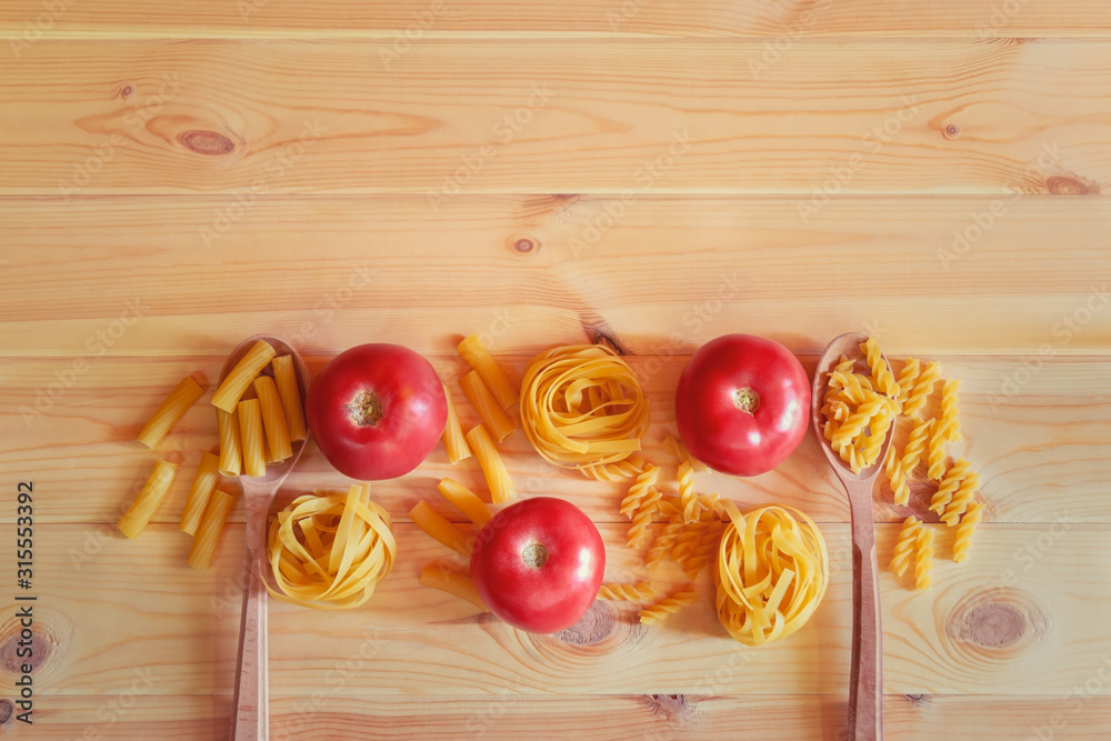 Border made of different kinds of raw pasta and fresh tomatoes on wooden background. Top view, copy space. Border made of different kinds of raw pasta and fresh tomatoes on wooden background. Top view, copy space.