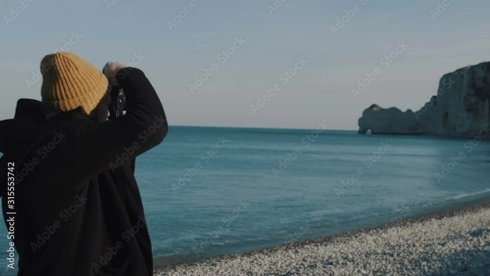 Happy excited Caucasian tourist man with camera exploring amazing sunny pebble sea beach at Etretat Normandy slow motion Happy excited Caucasian tourist man with camera exploring amazing sunny pebble sea beach at Etretat Normandy slow motion
