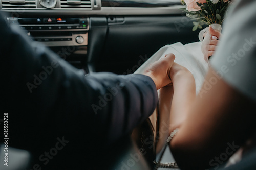 the bride and groom can not see the face hold tightly to the hand in the interior of the car from black leather on the background of a wedding bouquet photo