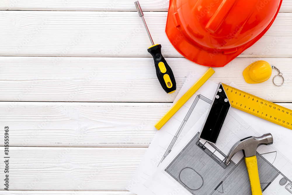 Builder work desk with hard hat, instruments and blueprints on white wooden background top-down frame copy space