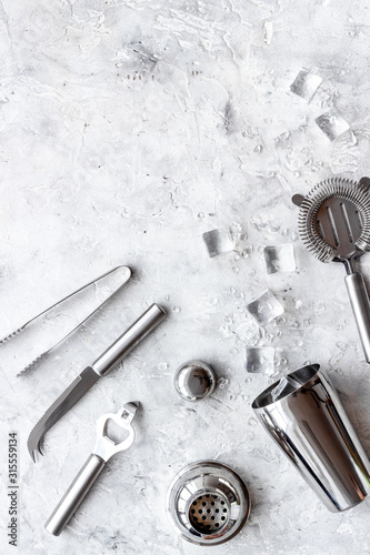 Bar utensil, tools - shaker, stainer - near ice cubes on grey background top-down frame copy space