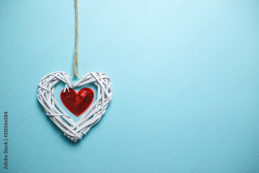 Big white wooden wicker heart with small red heart of sequins on the rope with copy space. Saint Valentine's day card on blue background.